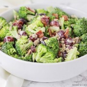 a white bowl filled broccoli salad with sliced grapes and pieces of bacon