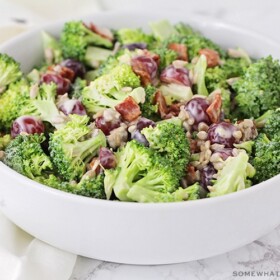 a white bowl filled broccoli salad with sliced grapes and pieces of bacon