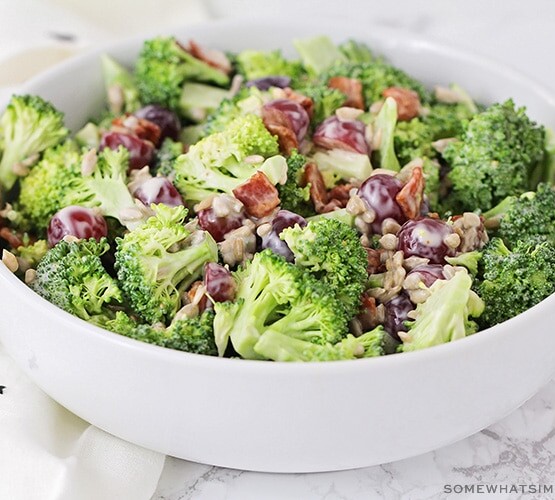 a white bowl filled broccoli salad with sliced grapes and pieces of bacon