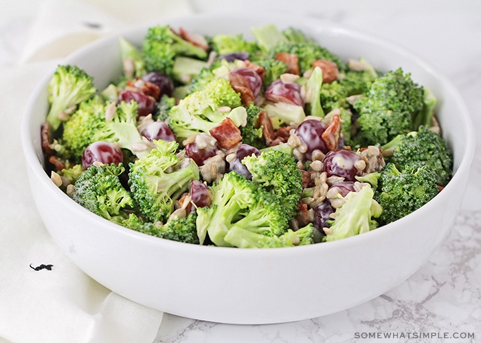 a white bowl filled broccoli salad with sliced grapes and pieces of bacon