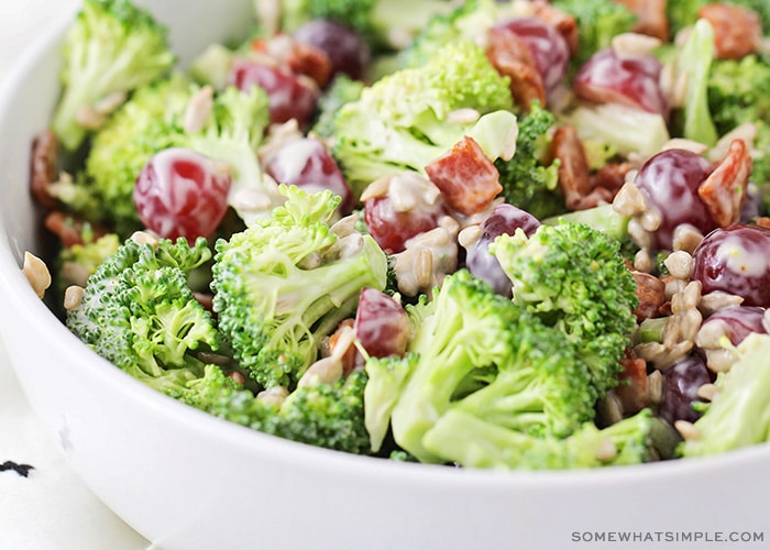 a close up of a bowl filled with pieces of broccoli, bacon, grapes topped with a dressing