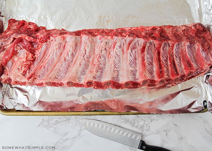 looking down on a full rack of raw ribs on a baking sheet lined with foil before going in the oven