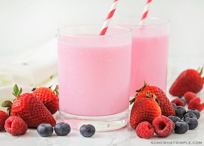 two glasses of a fizzy yogurt drink on a counter with pieces of fruit laying next to them