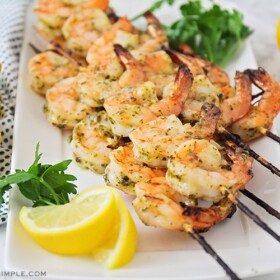 several skewers of grilled pesto shrimp fresh off the BBQ and laying on a white serving platter.