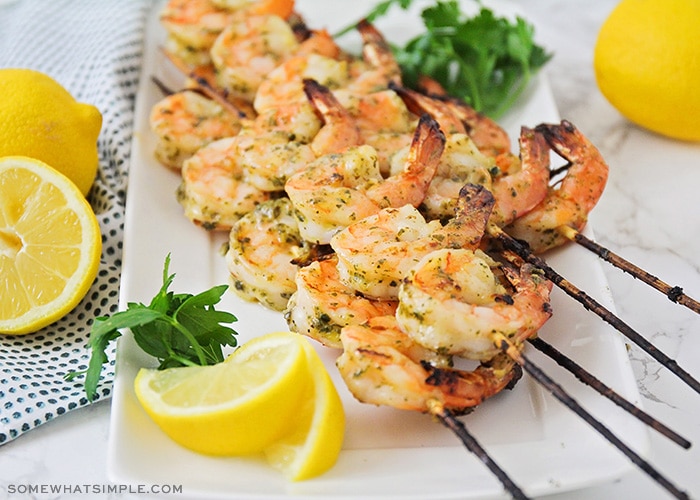 several skewers of grilled pesto shrimp fresh off the BBQ and laying on a white serving platter.