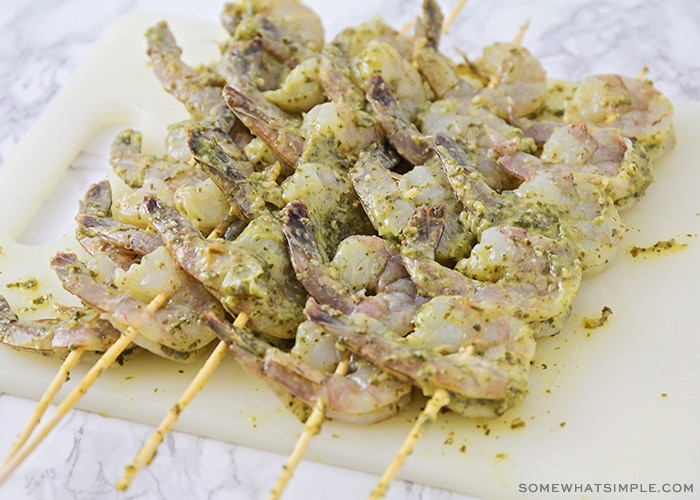 large raw shrimp that have been placed on wooden skewers and covered with a pesto marinade