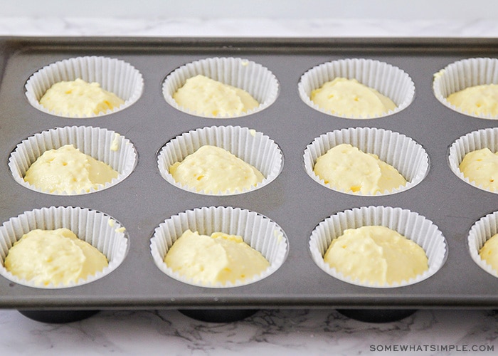a cupcake tin with white paper liners filled with lemon cupcake batter
