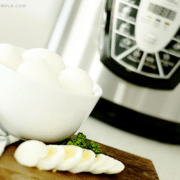 a bowl of hard boiled eggs in front of an instant pot. One of the eggs has been cut into slices and layed out on a cutting board in front of the bowl.