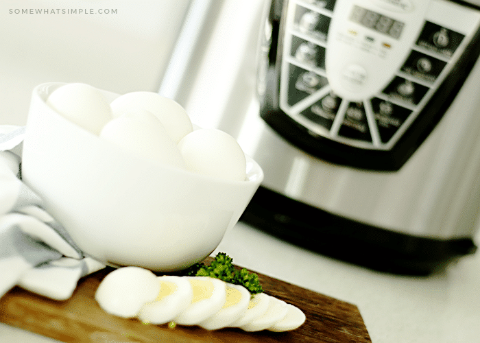 a bowl of hard boiled eggs in front of an instant pot. One of the eggs has been cut into slices and layed out on a cutting board in front of the bowl.