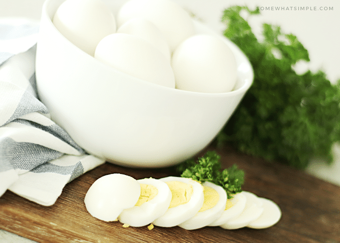 A close up of a bowl filled with eggs that have been hard boiled. One of the eggs has been sliced into several pieces and is laying in front of the bowl.