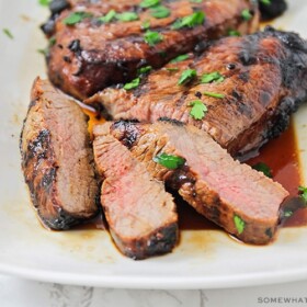 slices of steak that have been soaked in this quick steak marinade recipe on a white platter with juices pooling at the bottom of the platter.