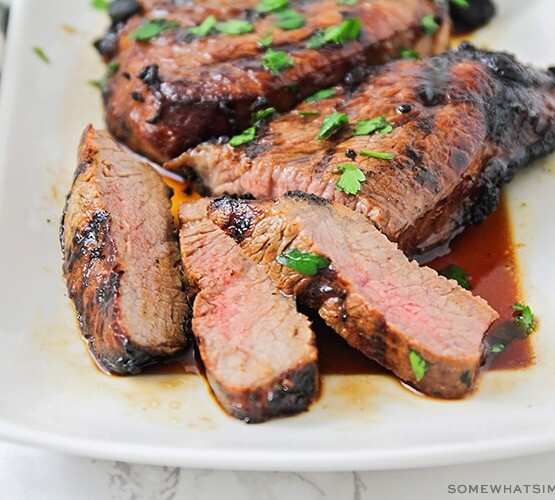 slices of steak that have been soaked in this quick steak marinade recipe on a white platter with juices pooling at the bottom of the platter.
