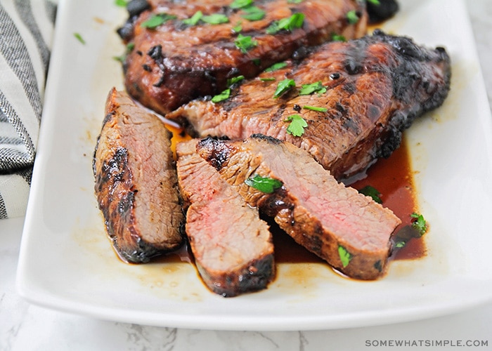 slices of steak that have been soaked in this quick steak marinade recipe on a white platter with juices pooling at the bottom of the platter.