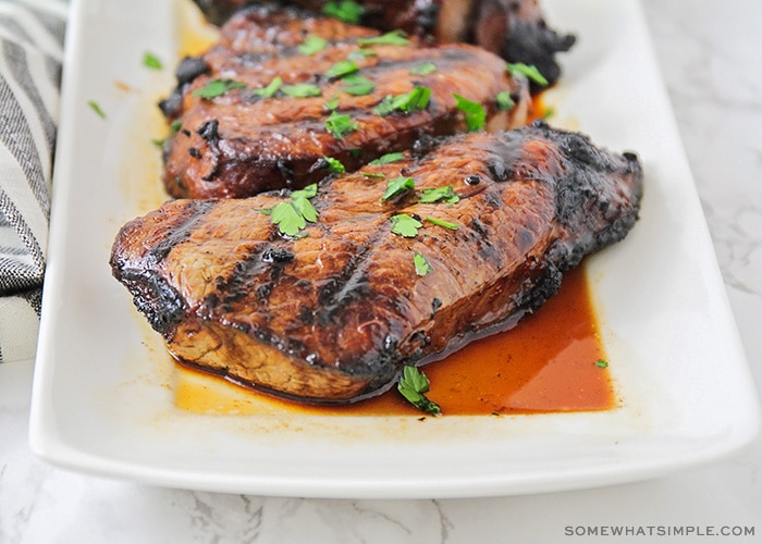 three pieces of steak that were grilled to perfection sitting on a white serving platter with marinade pooling on the tray.