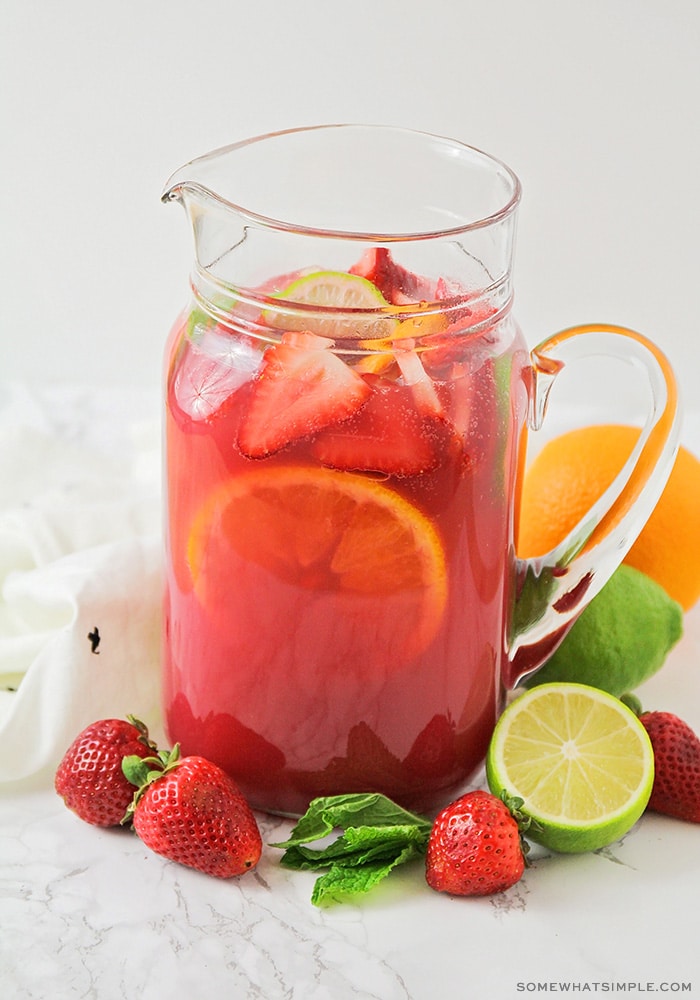 a glass pitcher filled with a red punch with slices of fruit floating inside.