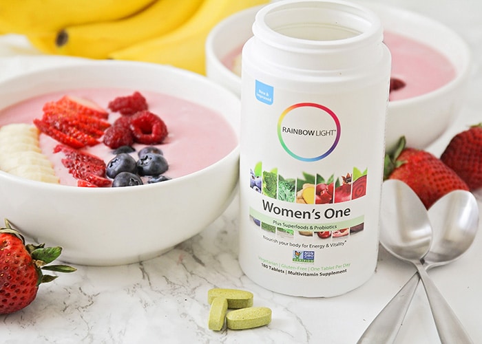 a smoothie bowl topped with fresh fruit next to vitamins