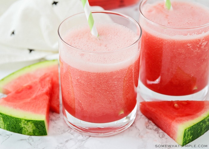 two glasses filled with this watermelon cooler recipe. Each glass has a green and white striped straw and slices of watermelon are next to the cups on the counter