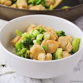 a white bowl filled with broccoli and chicken stir fry topped with chopped green onions all over a bed of white rice