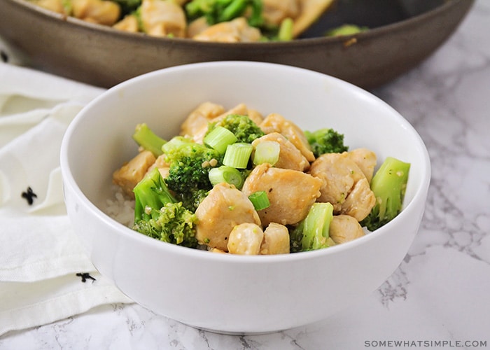 a white bowl filled with broccoli and chicken stir fry topped with chopped green onions all over a bed of white rice