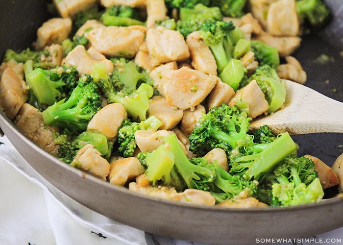 bite-sized pieces of chicken and broccoli in a black skillet being mixed by a wooden spoon