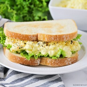 an egg salad sandwich on a white plate topped with lettuce on toasted white bread