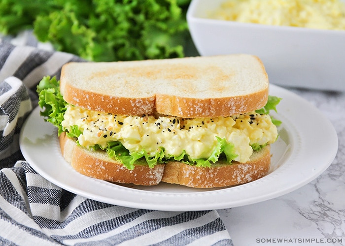 an egg salad sandwich on a white plate topped with lettuce on toasted white bread 