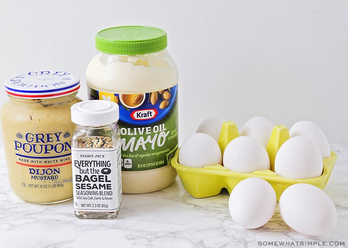 A bottle of Dijon mustard, mayo, eggs and a jar of seasoning on a counter