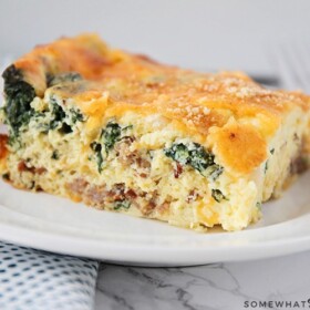 a square of spinach and egg casserole on a white plate. The casserole is topped with bread crumbs and cheese.