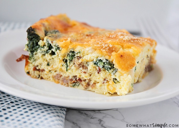 a square of spinach and egg casserole on a white plate. The casserole is topped with bread crumbs and cheese.