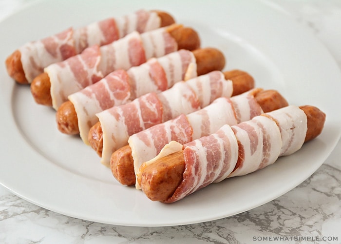 a plate of uncooked bacon wrapped hot dogs