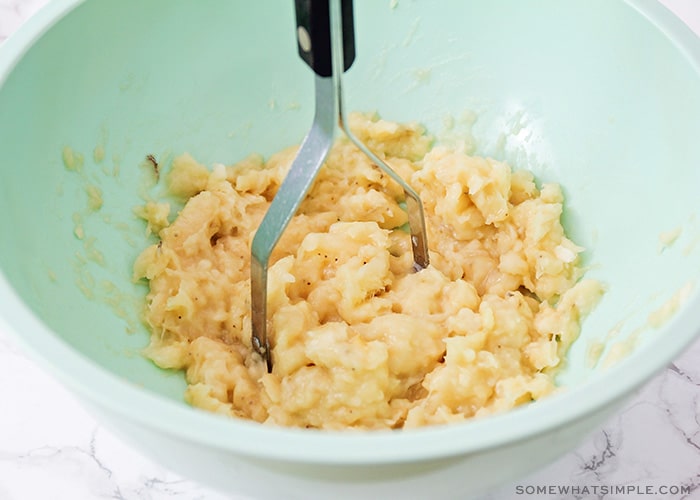 bananas being mashed in a light blue mixing bowl