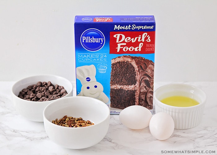 a box of devil's food cake mix, a bowl of chocolate chips, 2 eggs, a dish of oil and a bowl of chopped nuts
