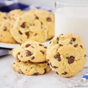 a few cake mix chocolate chip cookies on the counter next to a glass of milk with a plate full in the background.