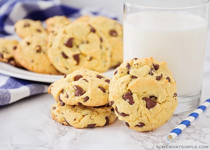 a few cake mix chocolate chip cookies on the counter next to a glass of milk with a plate full in the background.