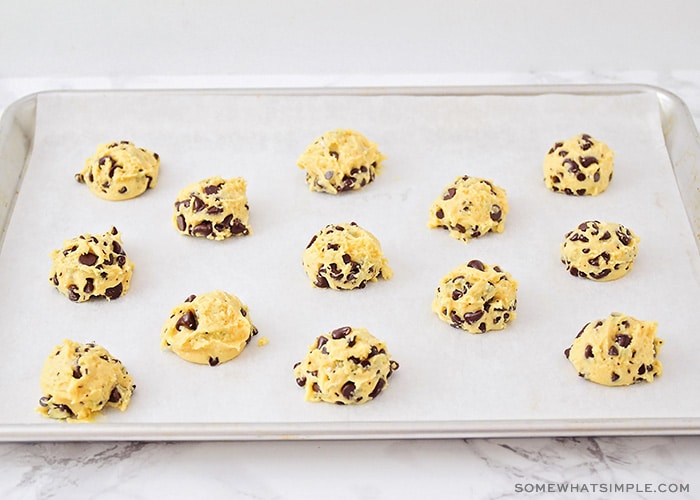 balls of chocolate chip cookie dough layed out on a baking sheet lined with parchment paper