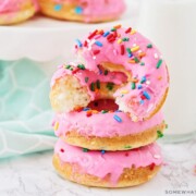 a stack of cake mix donuts, topped with pink icing and colored sprinkles. The donut on top has been cut in half.