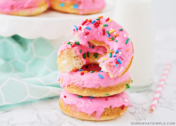 a stack of cake mix donuts, topped with pink icing and colored sprinkles. The donut on top has been cut in half.