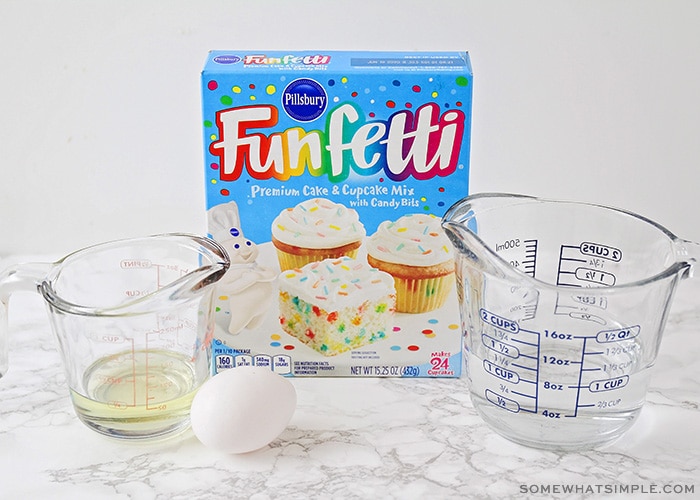 a box of funfetti cake mix on a counter next to a measuring cup of water, oil and an egg