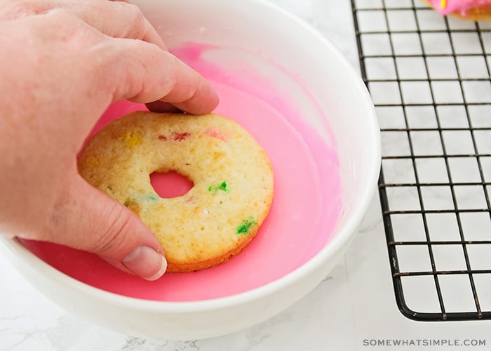 a hand dipping a donut into pink icing