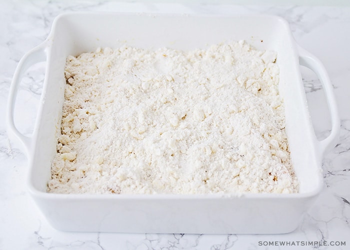 a white baking dish filled with peaches and a layer of cake mix is covering it