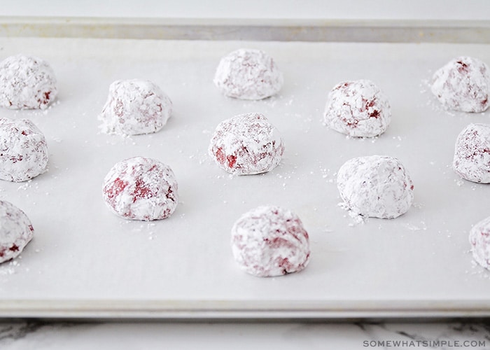 ball of cookie dough covered in powdered sugar on a baking sheet lined with parchment paper