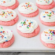 a cooking sheet filled with strawberry cake mix cookies topped with white frosting and colored sprinkles