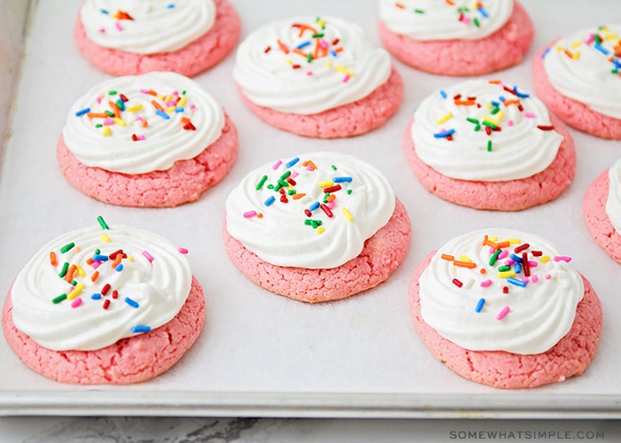 a cooking sheet filled with strawberry cake mix cookies topped with white frosting and colored sprinkles