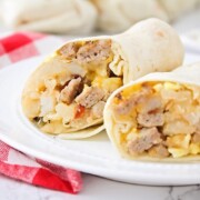 a breakfast burrito filled with potatoes, eggs, sausage and cheese that has been cut in half and is sitting on a white plate