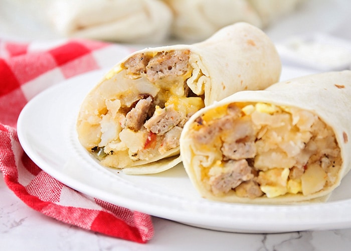 a breakfast burrito filled with potatoes, eggs, sausage and cheese that has been cut in half and is sitting on a white plate