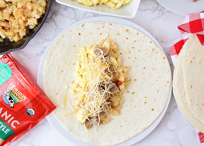 looking down on a tortilla with breakfast potatoes, eggs, cheese and sausage on top 