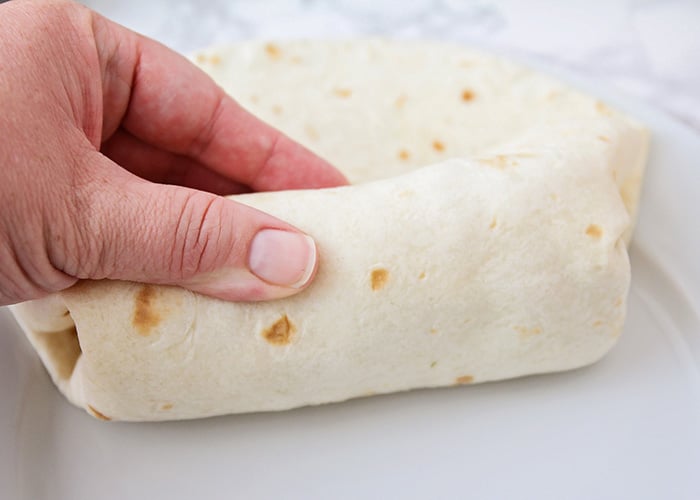 a hand holding a breakfast burrito that is being rolled up