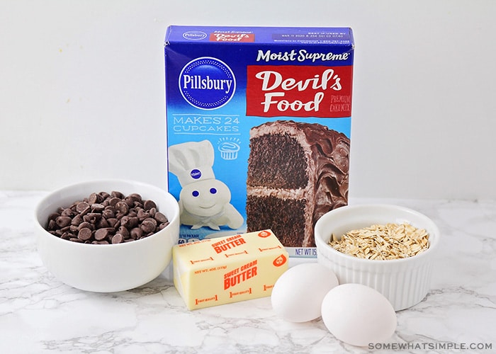 a box of Pillsbury Devil's Food cake mix, a bowl of chocolate chips, a stick of butter, two eggs and a small bowl of oats on a counter