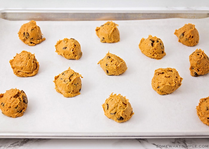 balls of pumpkin cookie dough with chocolate chips on a parchment lined cookie sheet