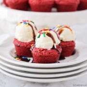 three small red velvet cake mix brownies on a stack of plates and topped with a scoop of ice cream, sprinkles and chocolate syrup